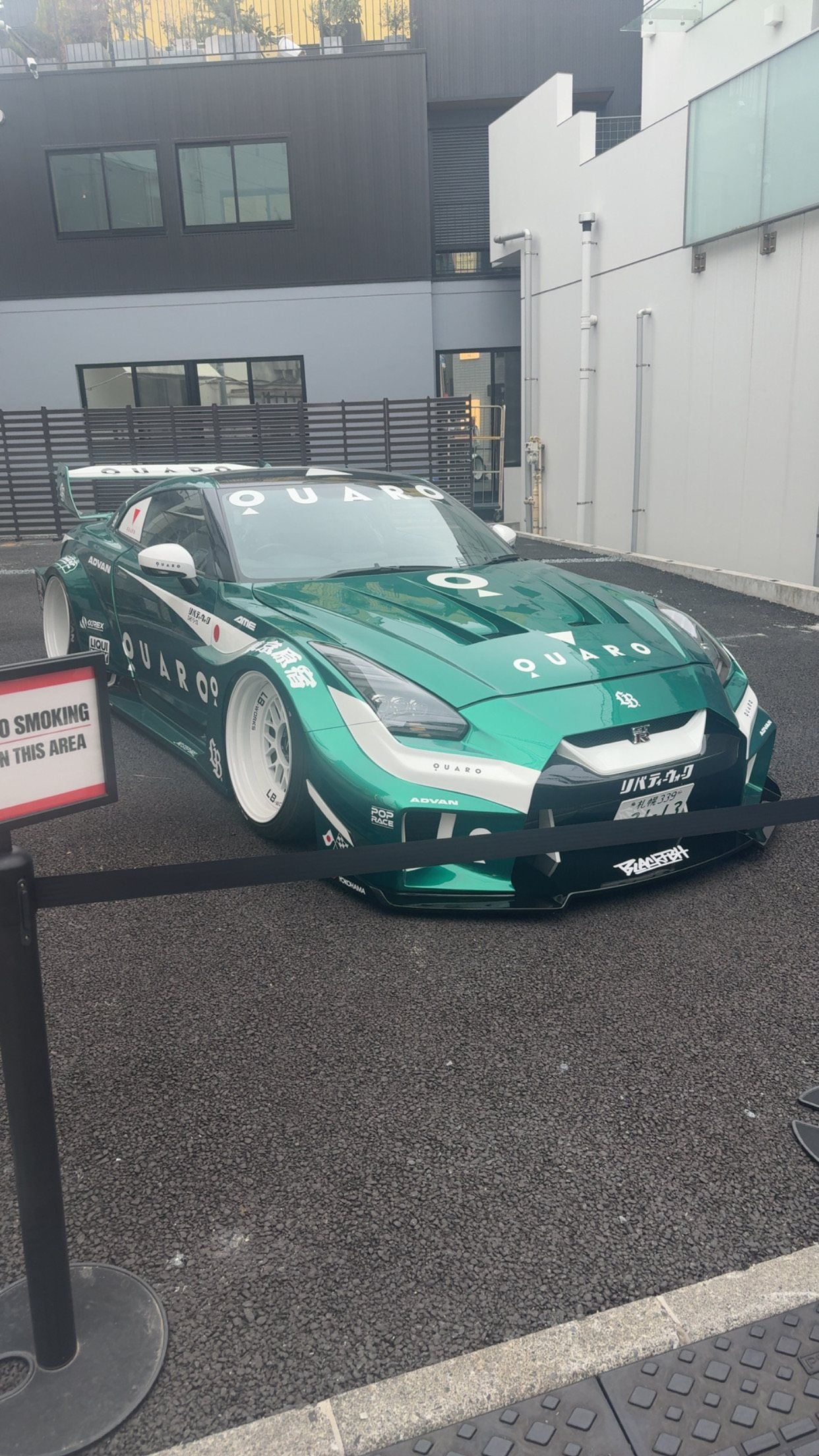 The green-and-white Liberty Walk widebody GT-R in QUARO livery on asphalt in overcast daylight